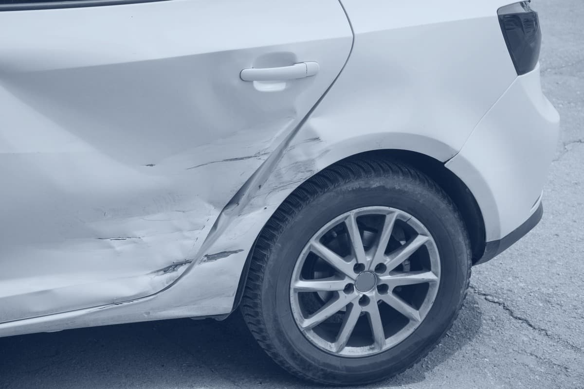 Rear quarter of a white sedan, a deep crease along the rear door and quarter panel above the wheel.